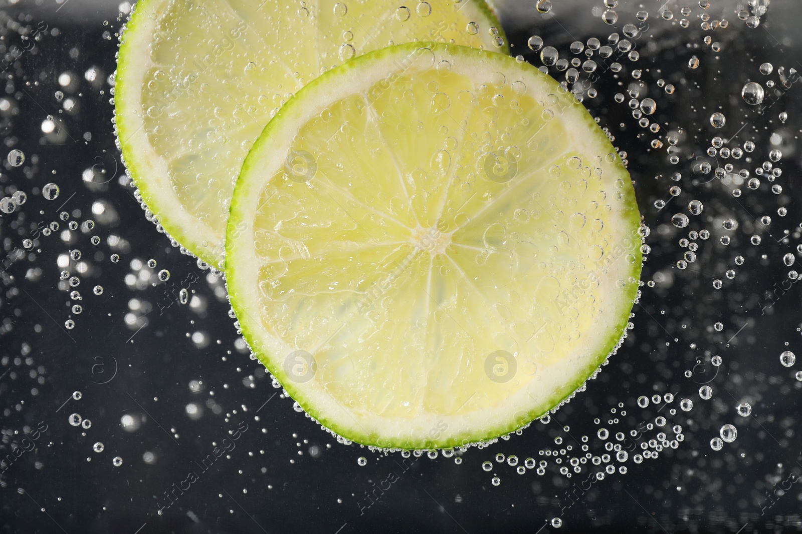 Photo of Juicy lime slices in soda water against black background, closeup