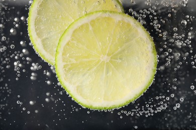 Juicy lime slices in soda water against black background, closeup