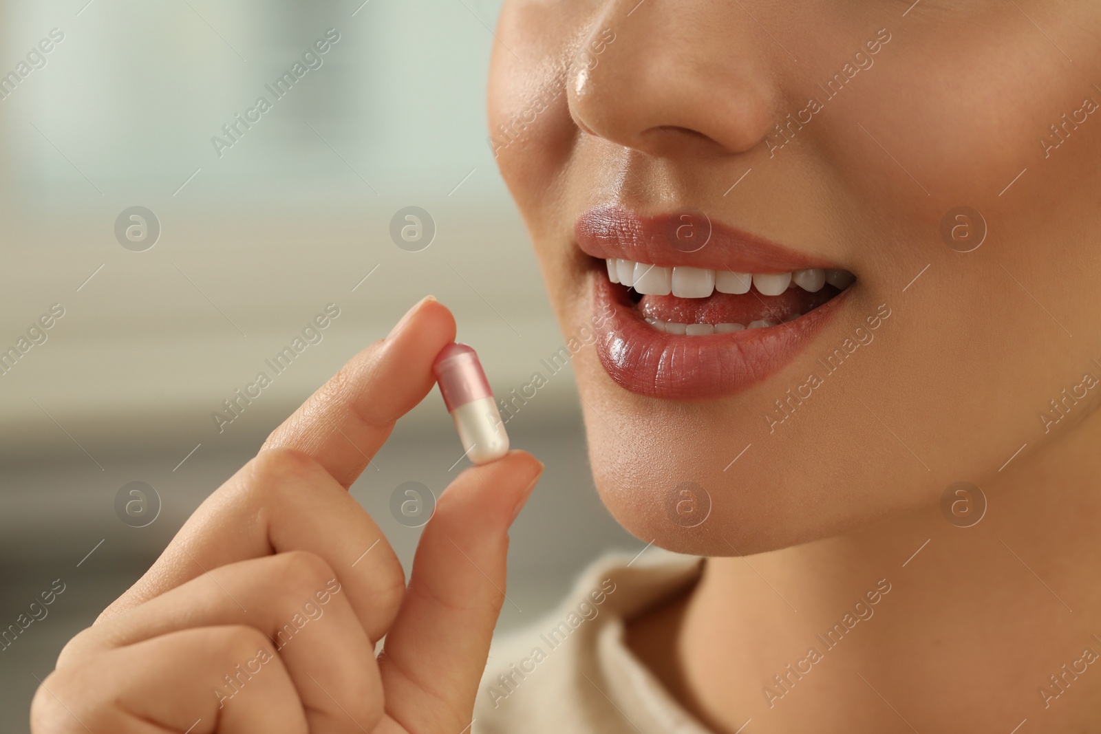 Photo of Young woman taking dietary supplement pill on blurred background, closeup