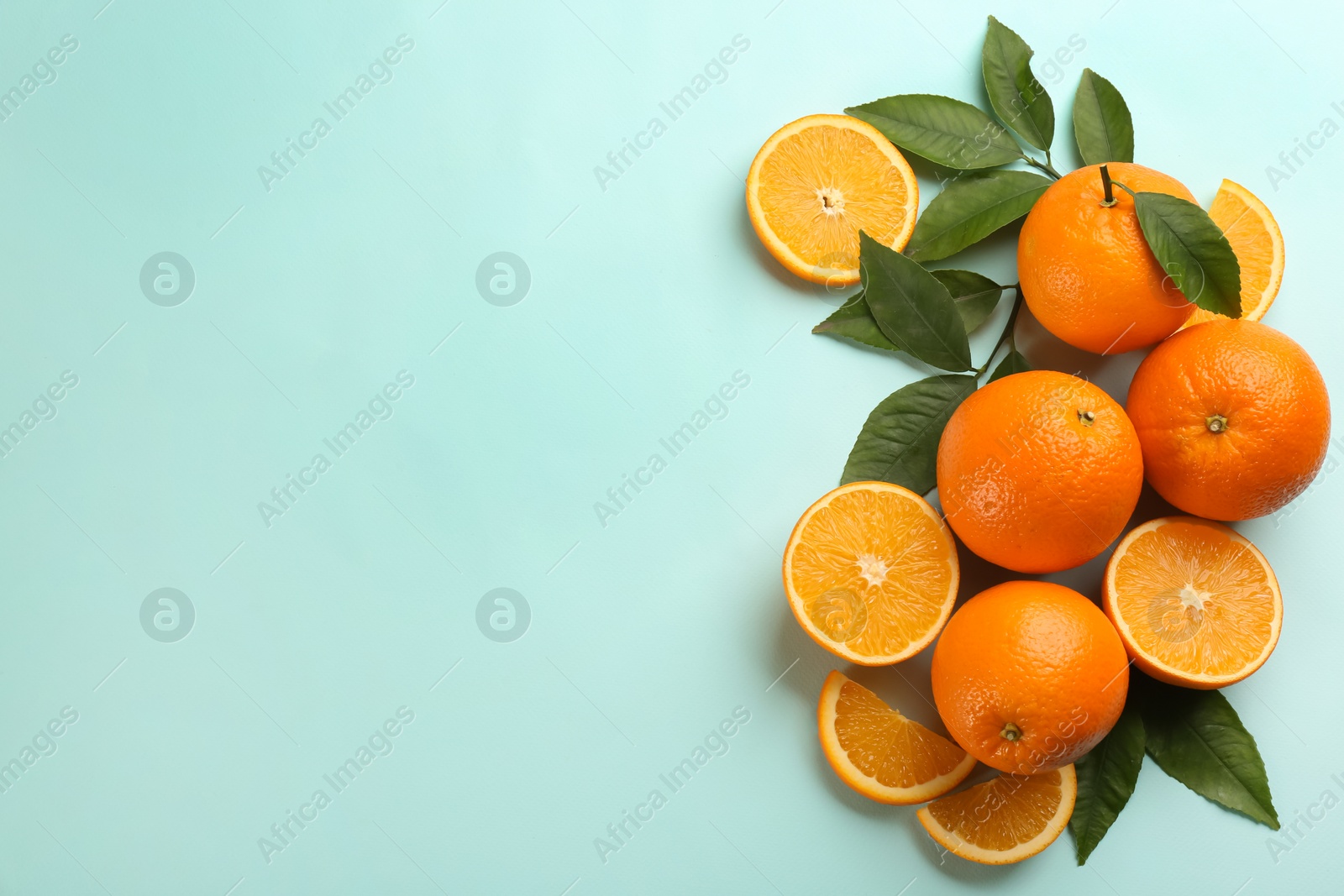 Photo of Fresh ripe oranges with green leaves on light blue background, flat lay. Space for text