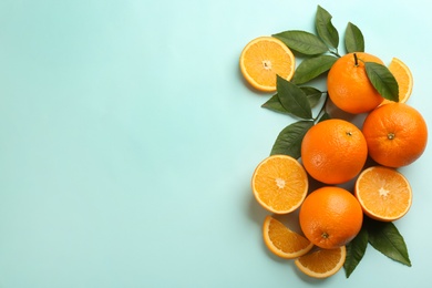 Photo of Fresh ripe oranges with green leaves on light blue background, flat lay. Space for text