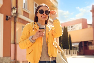 Photo of Happy young woman with coffee on city street in morning