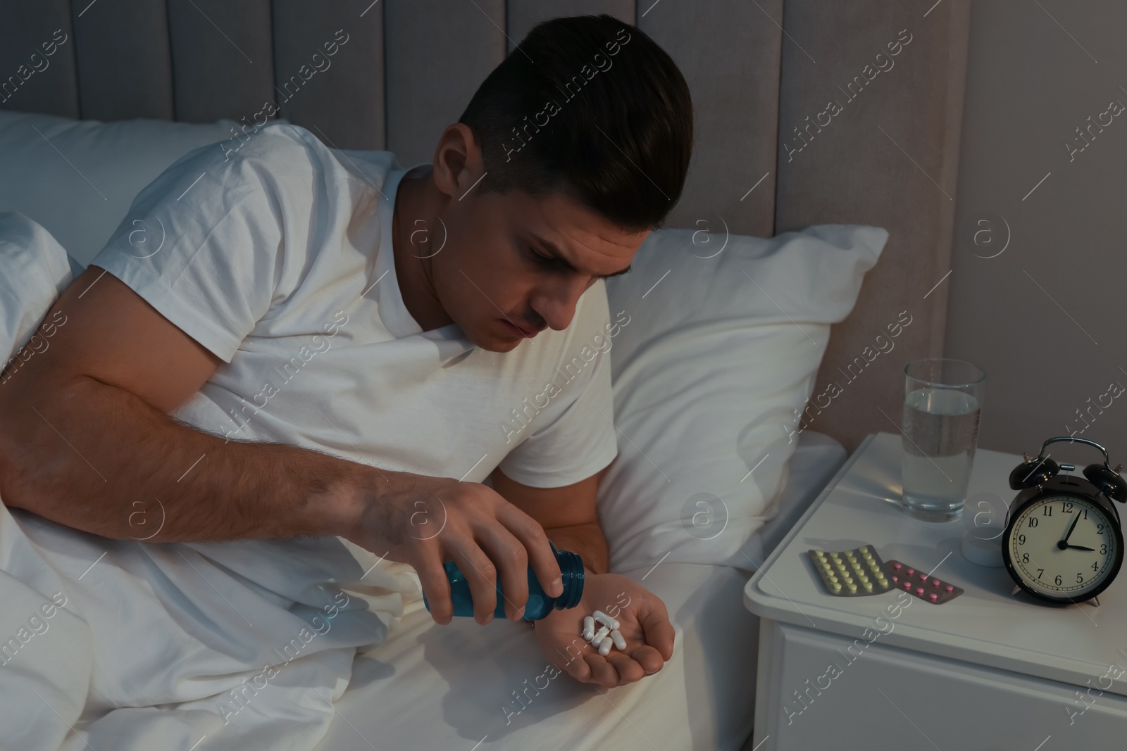 Photo of Man suffering from insomnia taking pills in bed at night