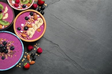 Photo of Acai smoothie bowls with granola and fruits on black table, flat lay. Space for text