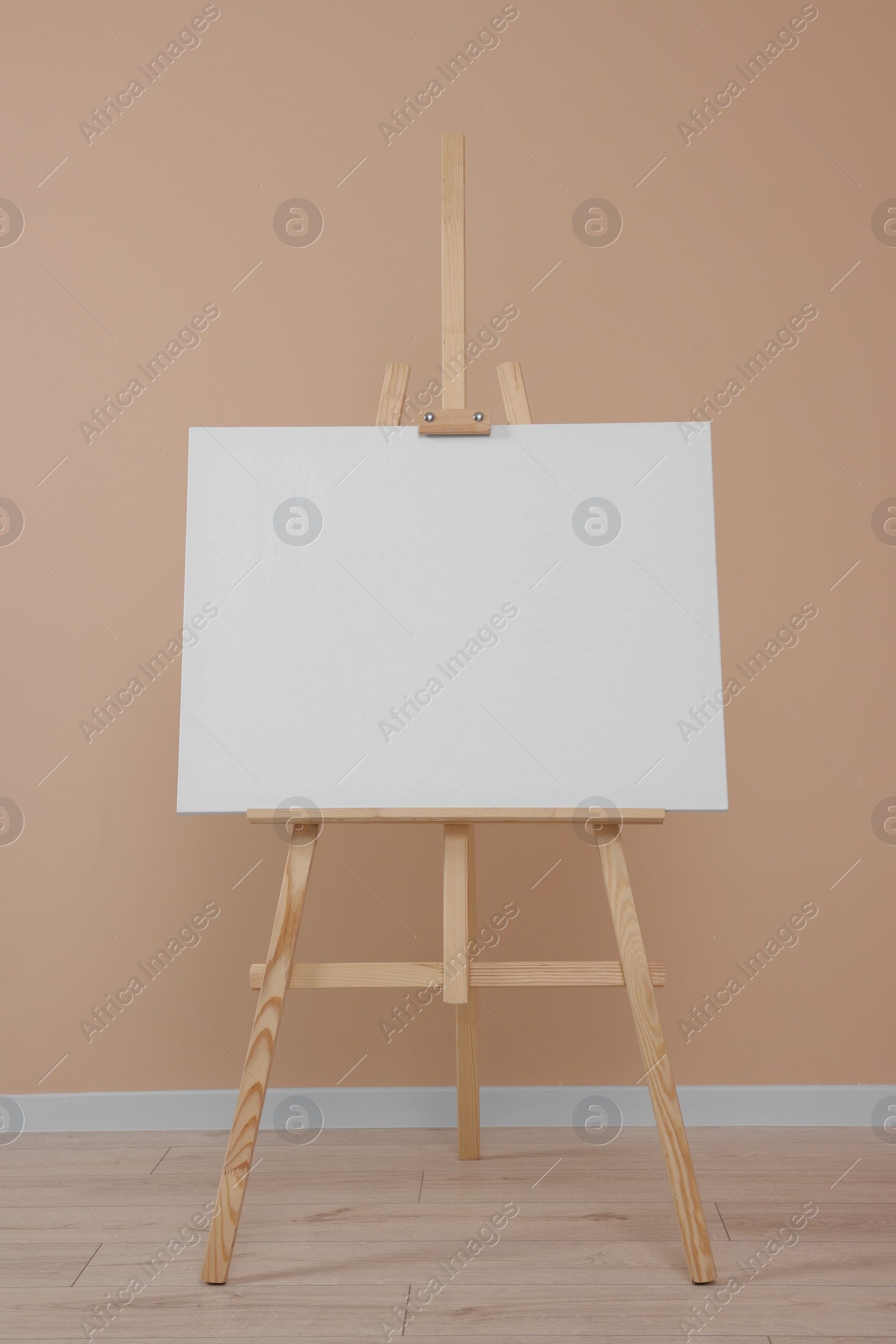 Photo of Wooden easel with blank canvas near beige wall indoors