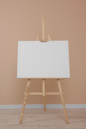 Wooden easel with blank canvas near beige wall indoors