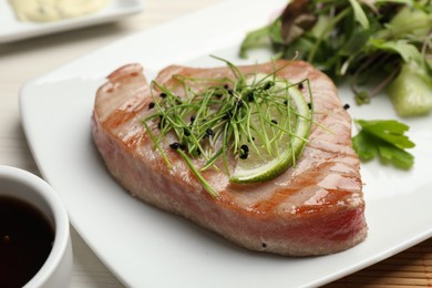 Photo of Delicious tuna steak with microgreens and lime on plate, closeup