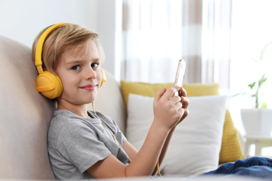 Cute little boy with headphones and smartphone listening to audiobook at home