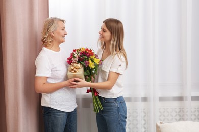 Photo of Young daughter congratulating her mom with flowers and gift at home. Happy Mother's Day