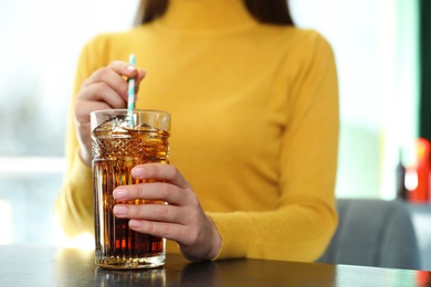 Photo of Woman with glass of refreshing cola at table indoors, closeup. Space for text