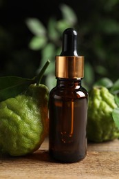 Photo of Glass bottle of bergamot essential oil and fresh fruits on wooden table