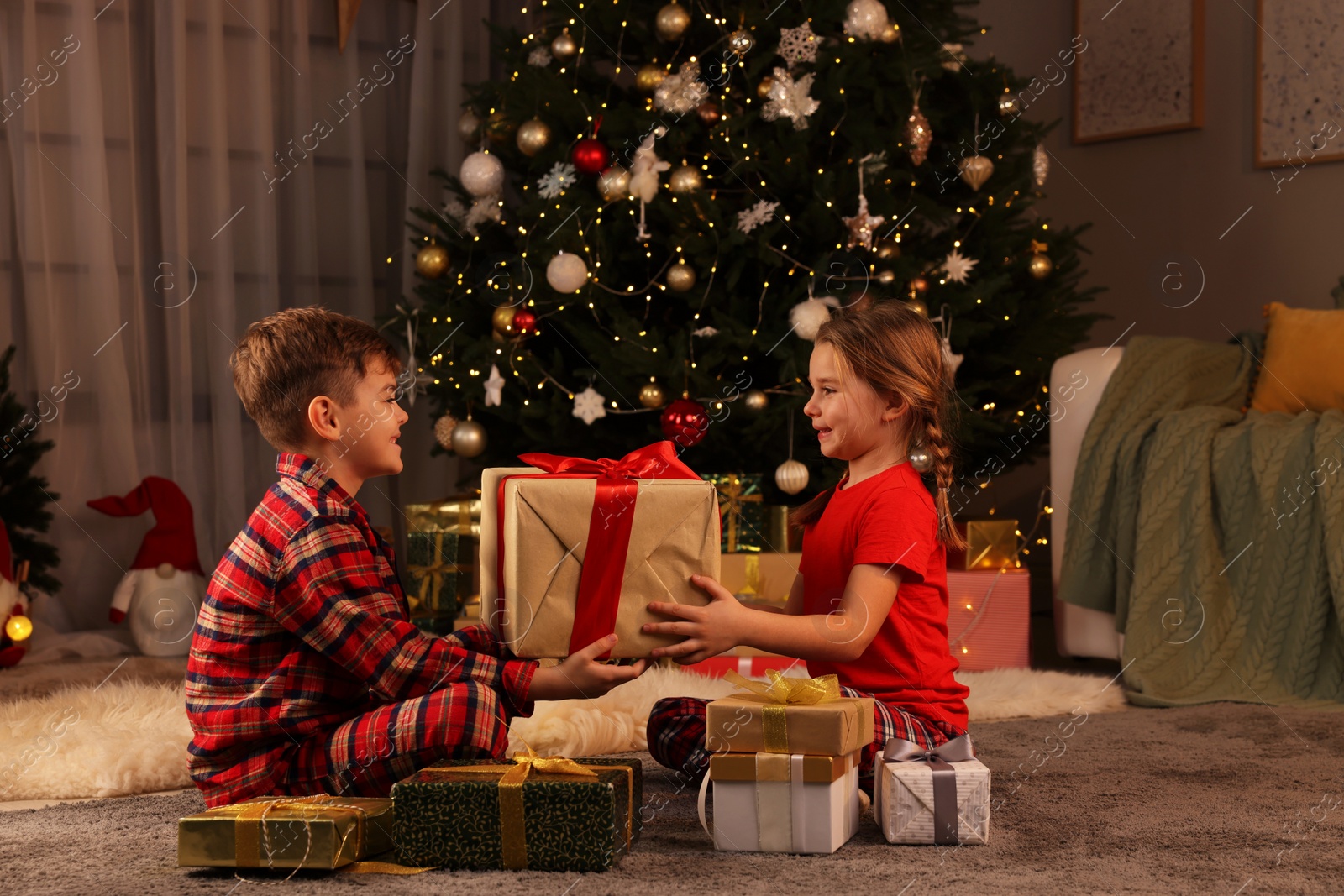 Photo of Cute little children with gift box near Christmas tree at home