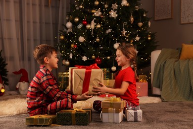 Photo of Cute little children with gift box near Christmas tree at home