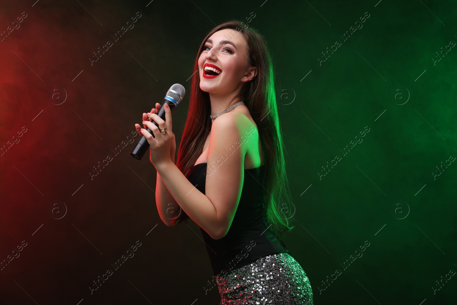 Photo of Emotional woman with microphone singing in color lights on dark background