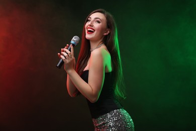 Photo of Emotional woman with microphone singing in color lights on dark background