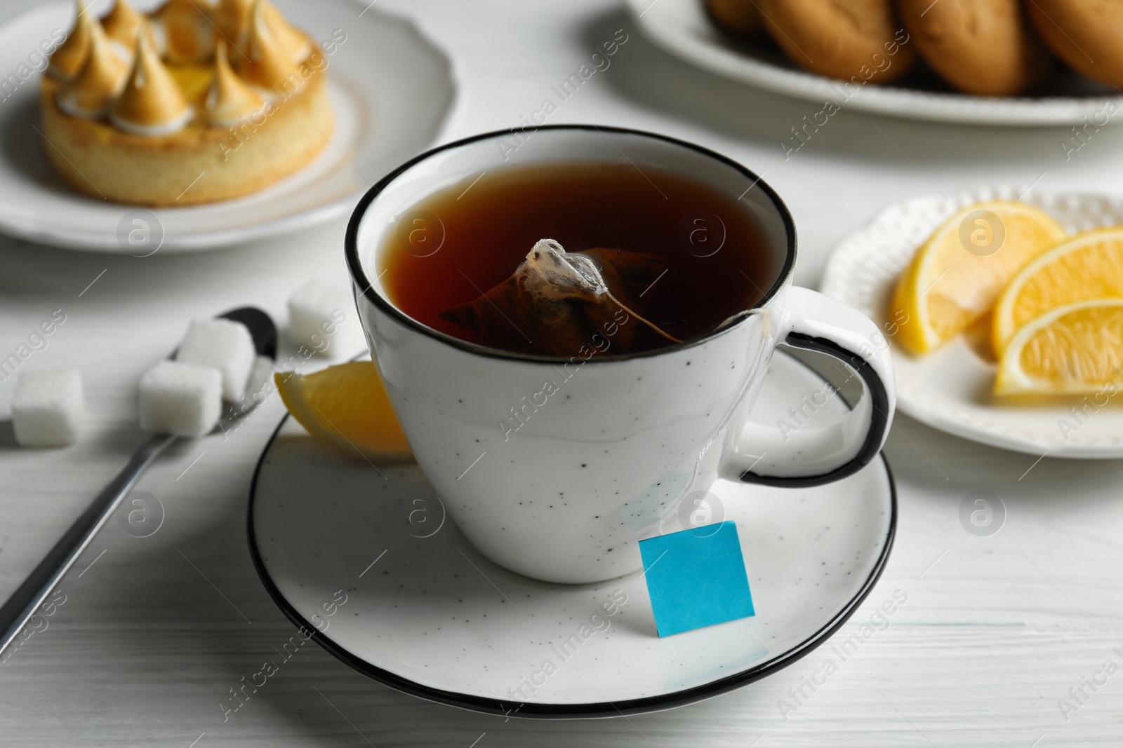 Photo of Tea bag in cup of hot water and lemon on white wooden table