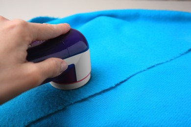 Woman using fabric shaver on light blue cloth with lint, closeup. Space for text