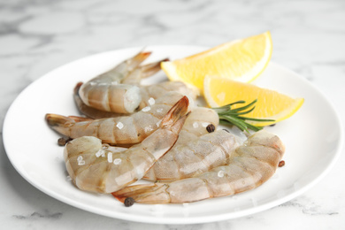 Photo of Fresh raw shrimps with lemon and rosemary on marble table