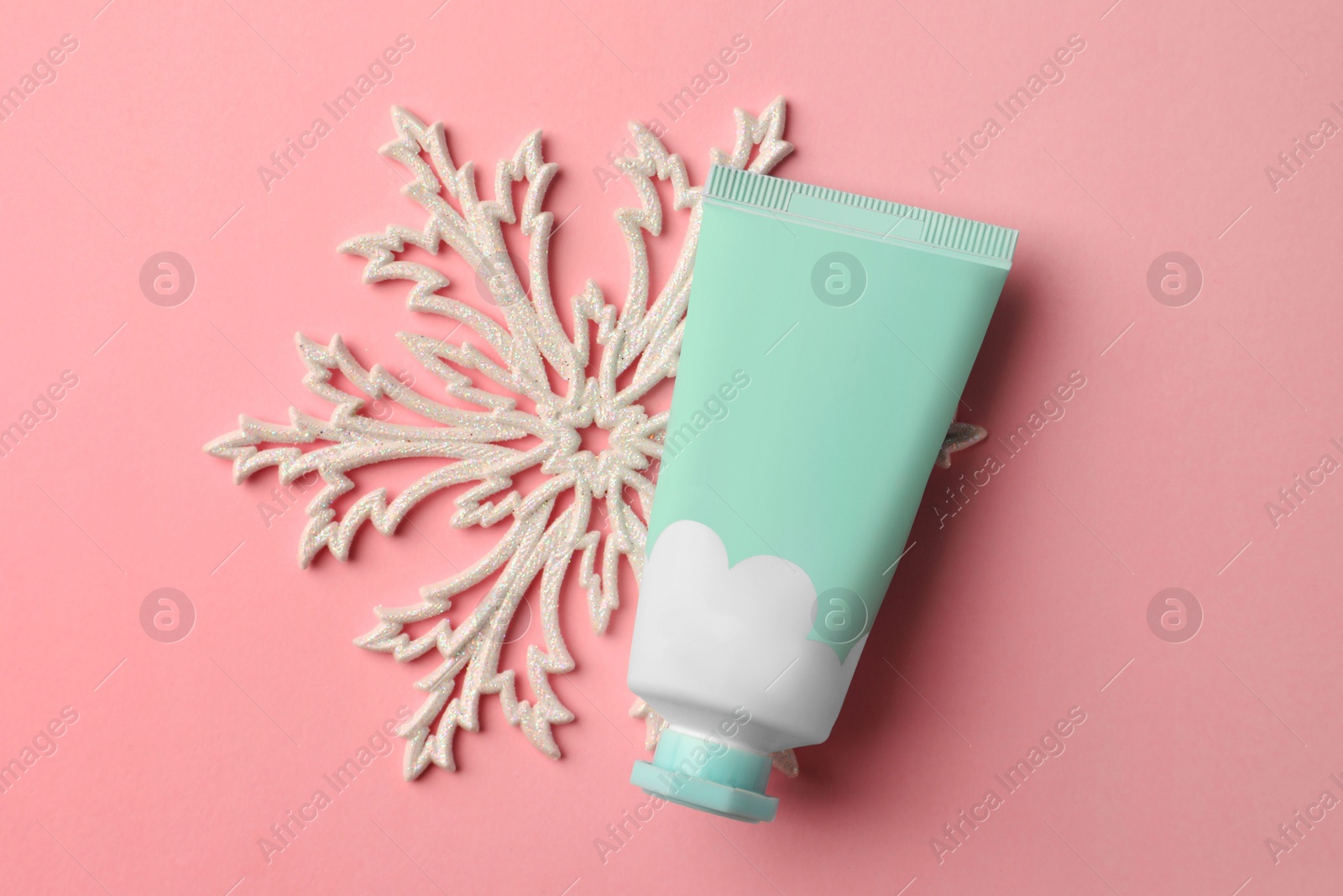 Photo of Winter skin care. Hand cream and snowflake on pink background, top view