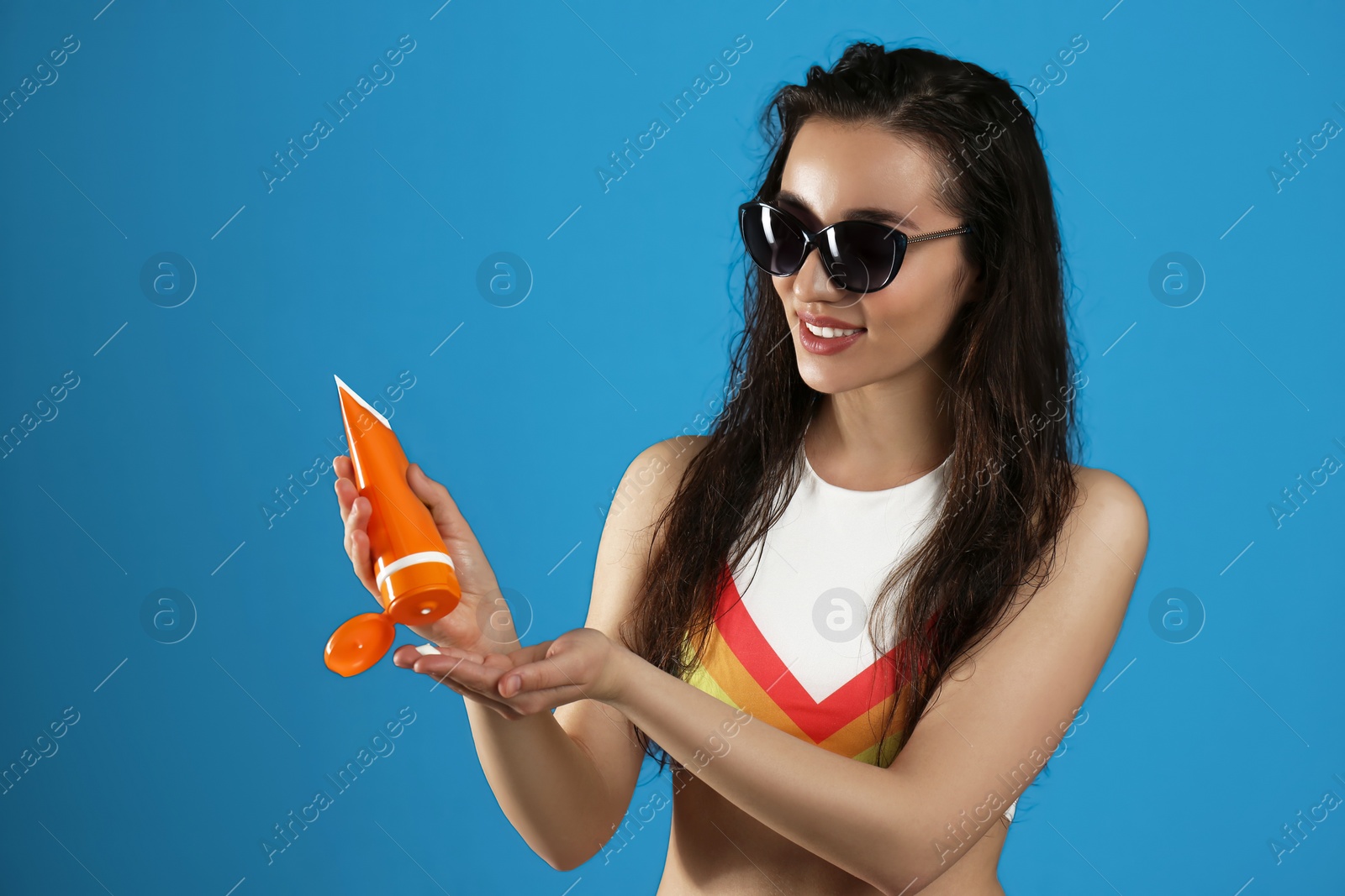 Photo of Young woman applying sun protection cream on dark blue background