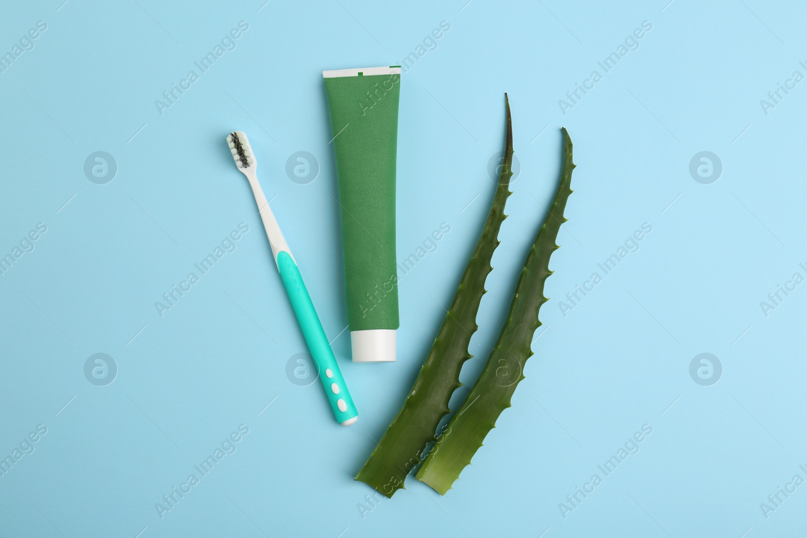 Photo of Tube of toothpaste, toothbrush and fresh aloe on light blue background, flat lay