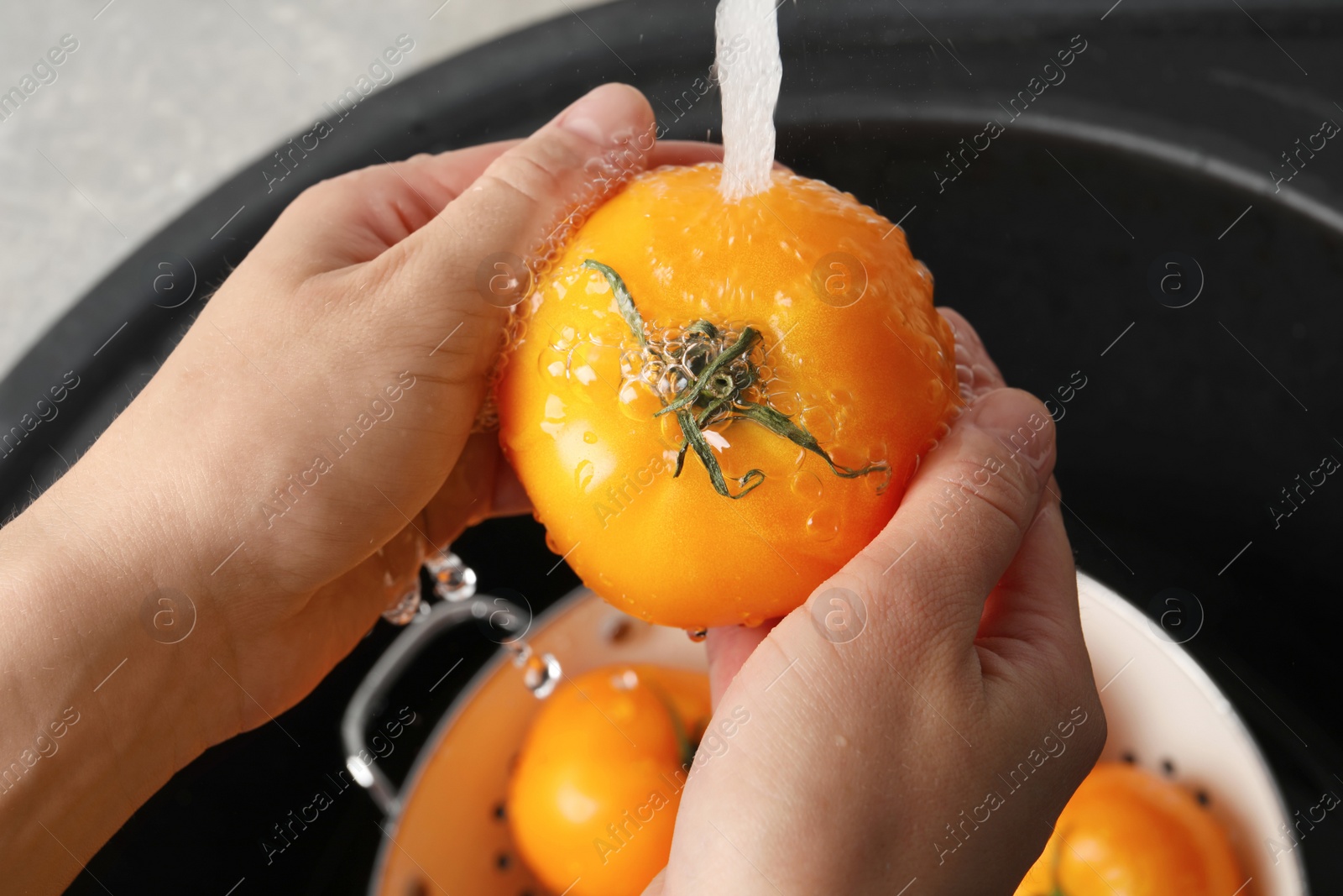Photo of Woman washing fresh ripe yellow tomatoes, closeup
