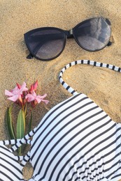 Photo of Beautiful sunglasses, swimsuit and tropical flower on sand
