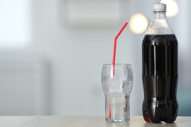 Photo of Bottle of cola and glass with ice on table against blurred background. Space for text