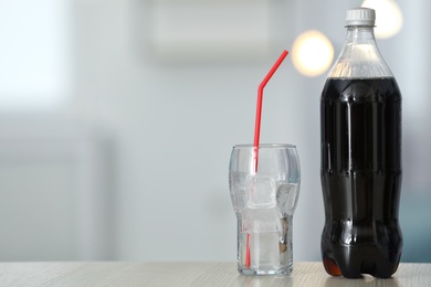 Bottle of cola and glass with ice on table against blurred background. Space for text