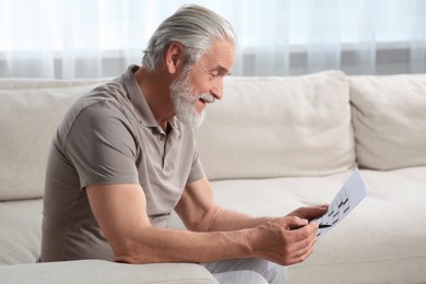 Senior man solving crossword on sofa at home