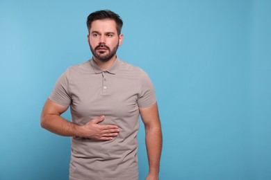 Photo of Man suffering from stomach pain on light blue background, space for text
