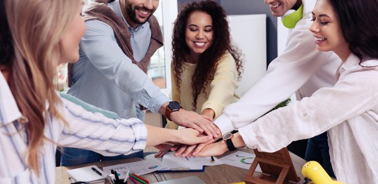 Image of Group of coworkers putting hands together in office. Banner design