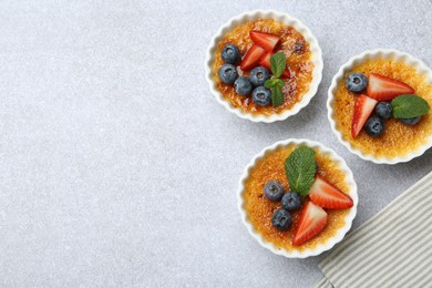 Photo of Delicious creme brulee with berries and mint in bowl on grey textured table, top view. Space for text