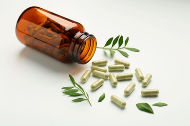 Bottle, vitamin capsules and leaves on white background