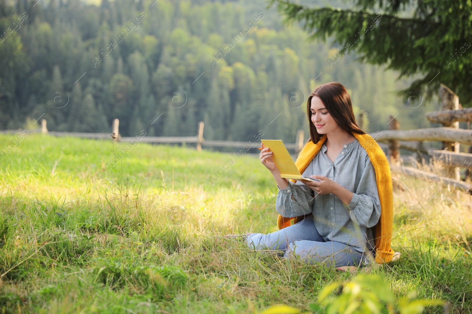 Photo of Beautiful young woman drawing with pencil in notepad on green grass