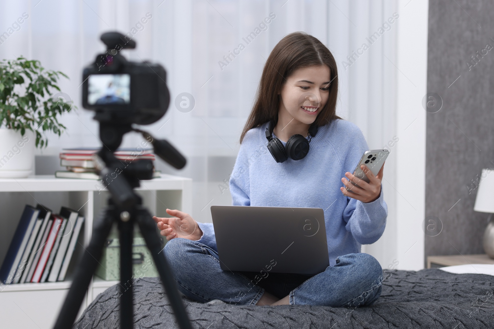 Photo of Smiling teenage blogger with laptop and smartphone streaming at home