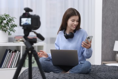 Smiling teenage blogger with laptop and smartphone streaming at home