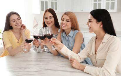 Photo of Beautiful young ladies clinking glasses of wine in kitchen. Women's Day