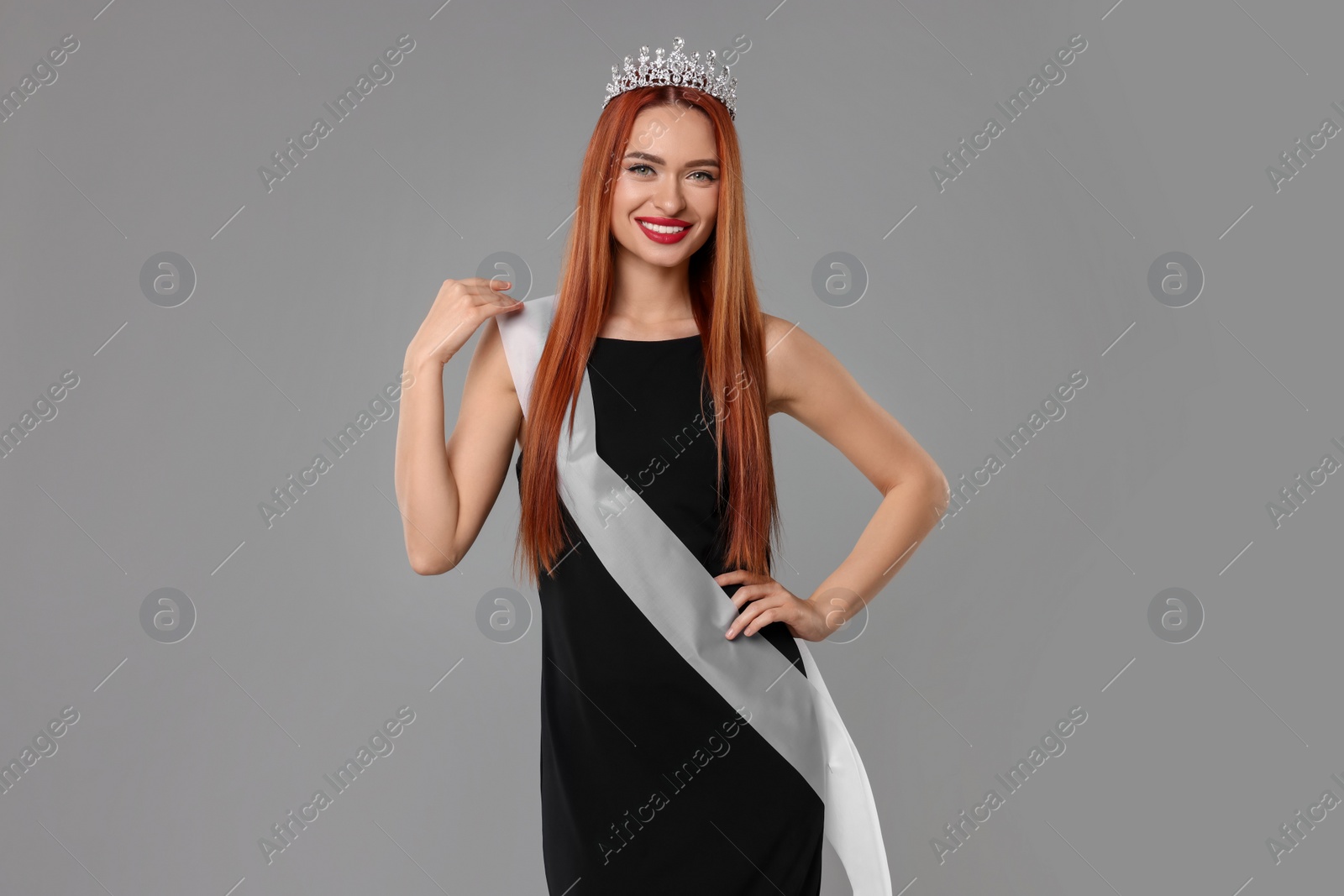 Photo of Beautiful young woman with tiara and ribbon in dress on light grey background. Beauty contest