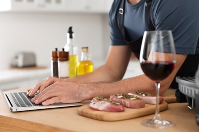 Photo of Man making dinner while watching online cooking course via laptop in kitchen, closeup