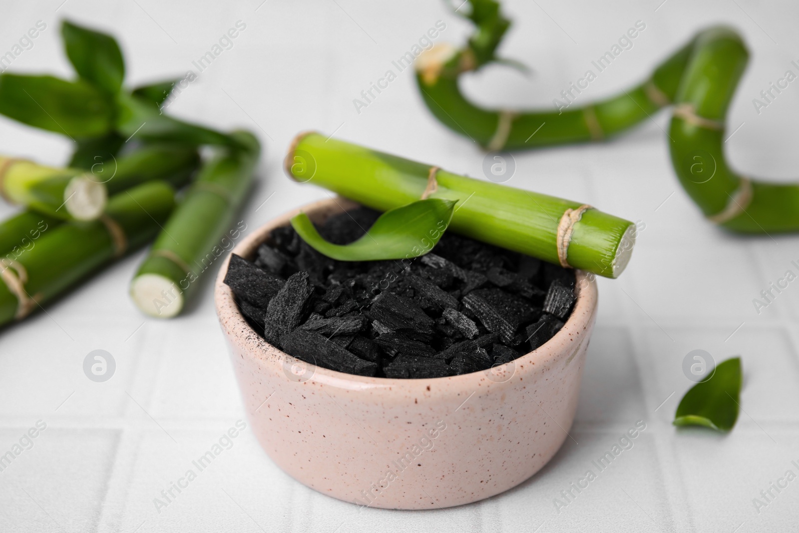 Photo of Fresh bamboo and charcoal on white tiled table, closeup