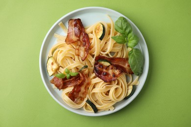 Photo of Tasty pasta with bacon and basil on light green table, top view