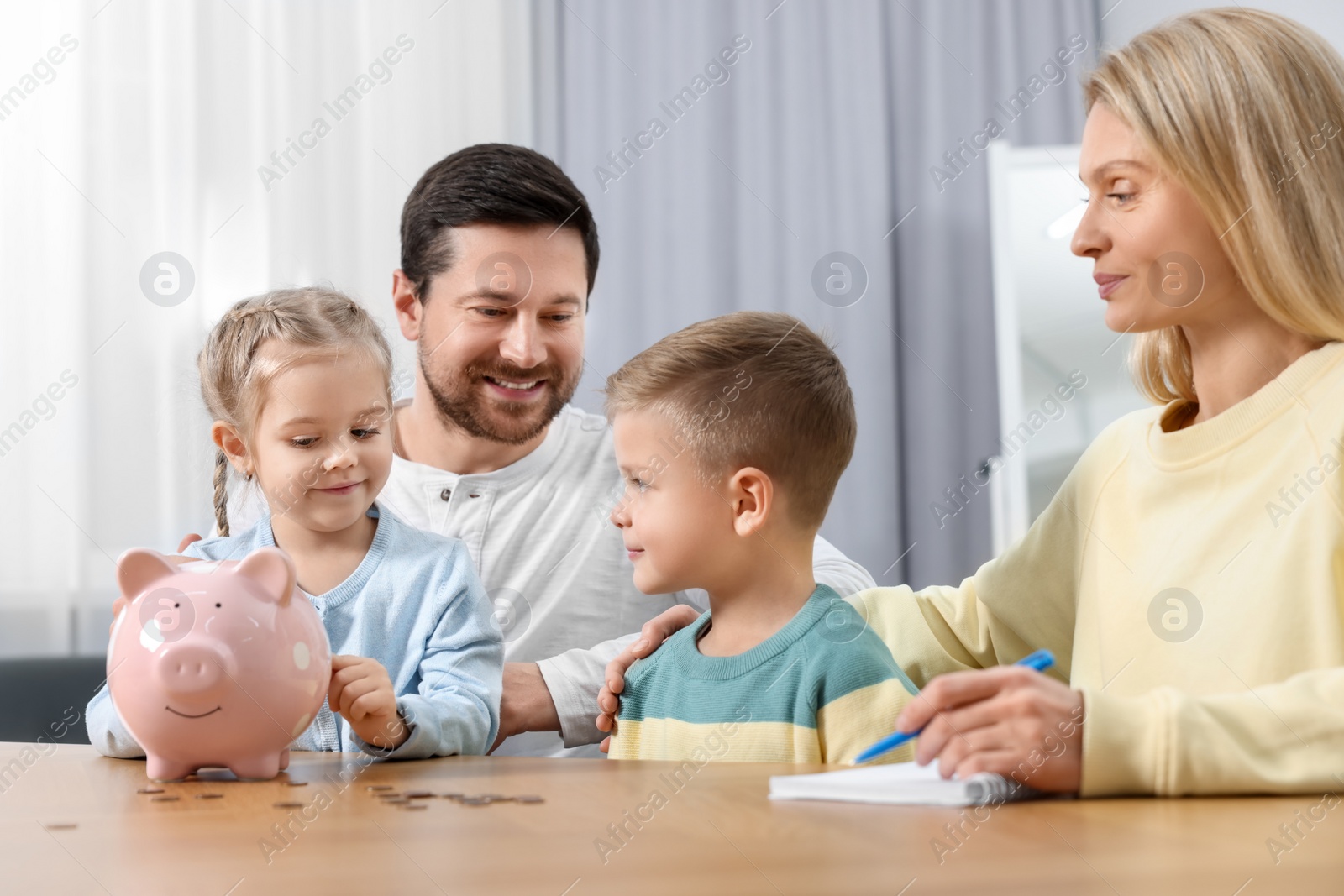 Photo of Planning budget together. Little girl with her family putting coins into piggybank indoors