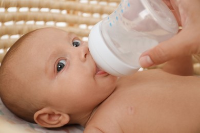 Photo of Mother giving her cute little baby drink from bottle in cradle, closeup