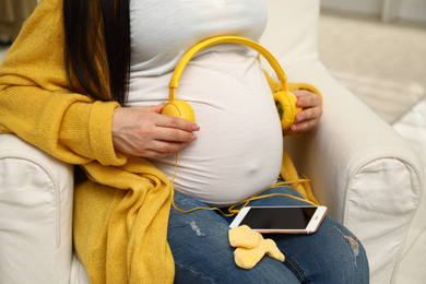 Photo of Pregnant woman with headphones and smartphone at home, closeup
