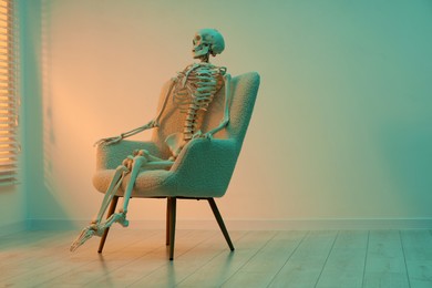 Waiting concept. Human skeleton sitting in armchair indoors