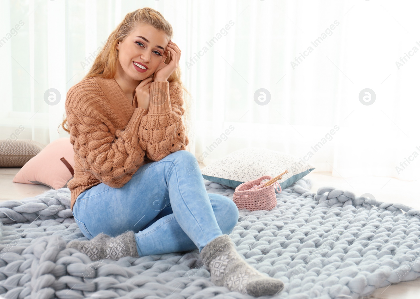Photo of Attractive young woman in cozy warm sweater sitting on floor at home. Space for text