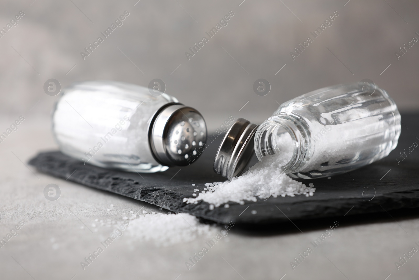 Photo of Natural salt in shakers on grey table, closeup