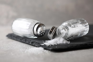 Natural salt in shakers on grey table, closeup