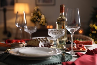 Photo of Christmas table setting with bottle of wine, appetizers and dishware indoors